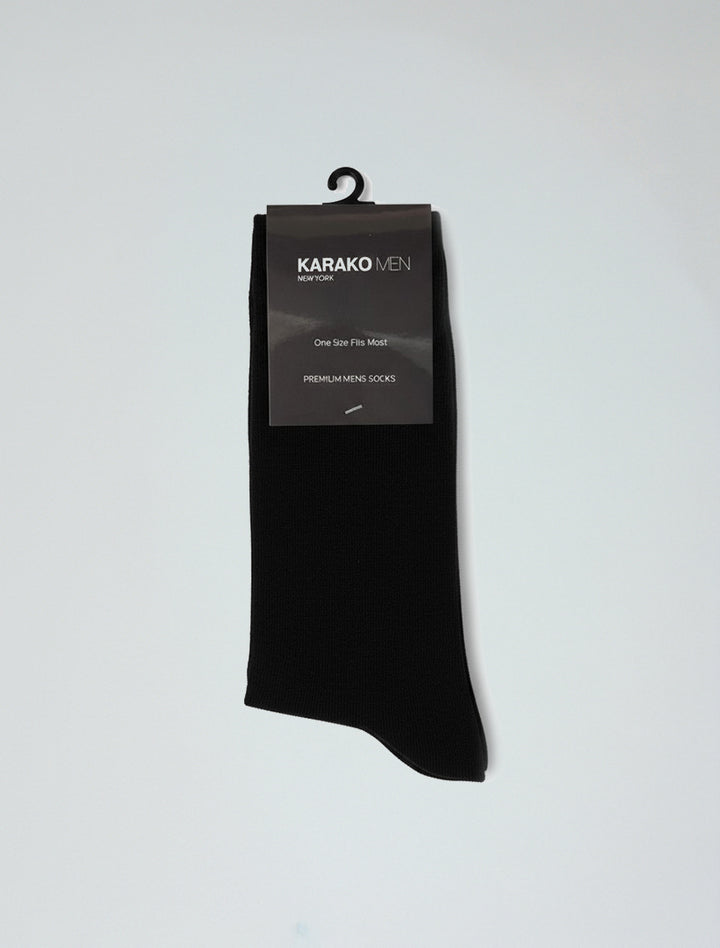 A pair of Karako Men Onyx Black Basic Dress Socks in retail packaging labeled "KARAKO MEN," featuring ribbed cuffs, elastic stretch for comfort, a hanging hook, and a "One Size Fits Most" tag.