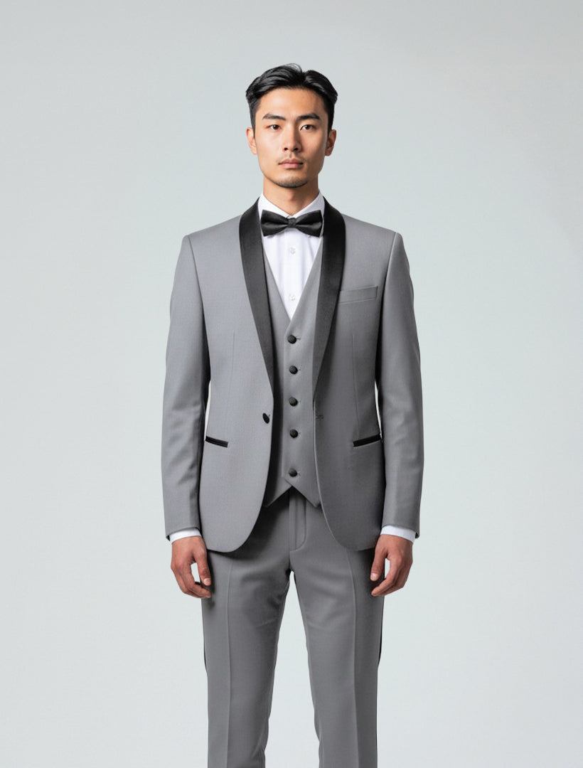 A man stands facing forward, wearing the Gino Vitale Men's Light Grey Shawl Lapel Tailored Fit Tuxedo with a white dress shirt, black bowtie, and matching vest against a plain background.
