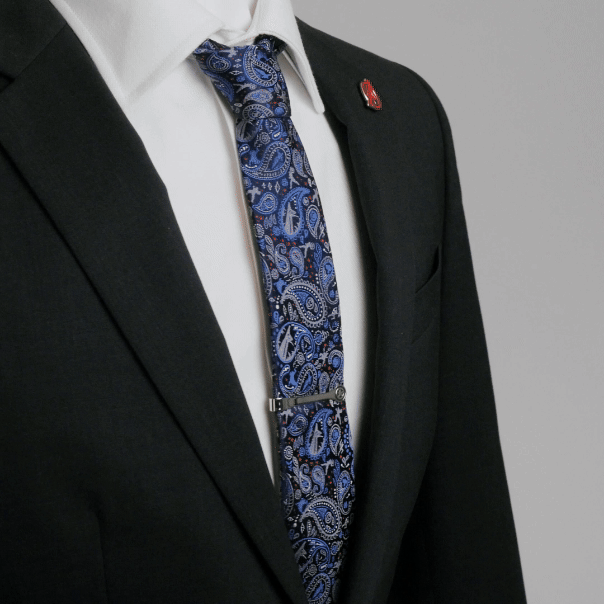 A person in a black suit wears a patterned blue tie with a tie bar and a Marvel Avengers Lapel Pin on their lapel.