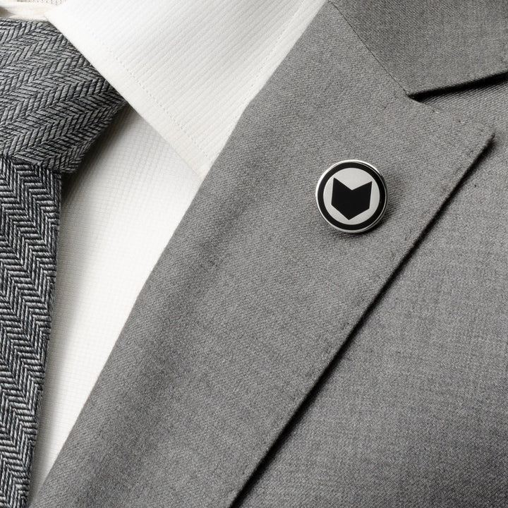 A circular Marvel Hawkeye Lapel Pin featuring a black arrowhead icon on a white background, pinned to the lapel of a gray suit jacket.