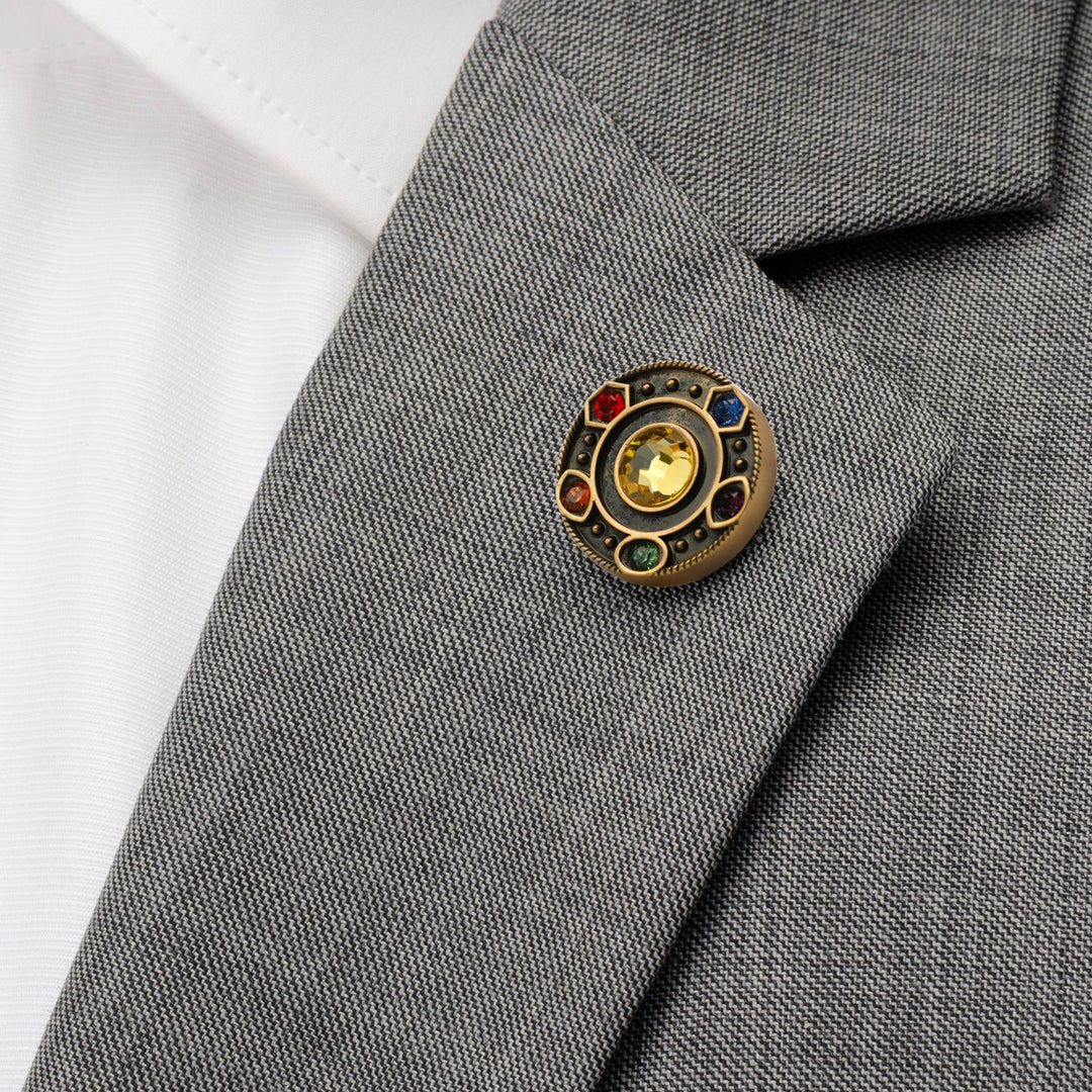 Marvel Avengers Infinity Stones Antique Gold Lapel Pin featuring a circular gold design with six colored stones, pinned to the lapel of a grey suit jacket.