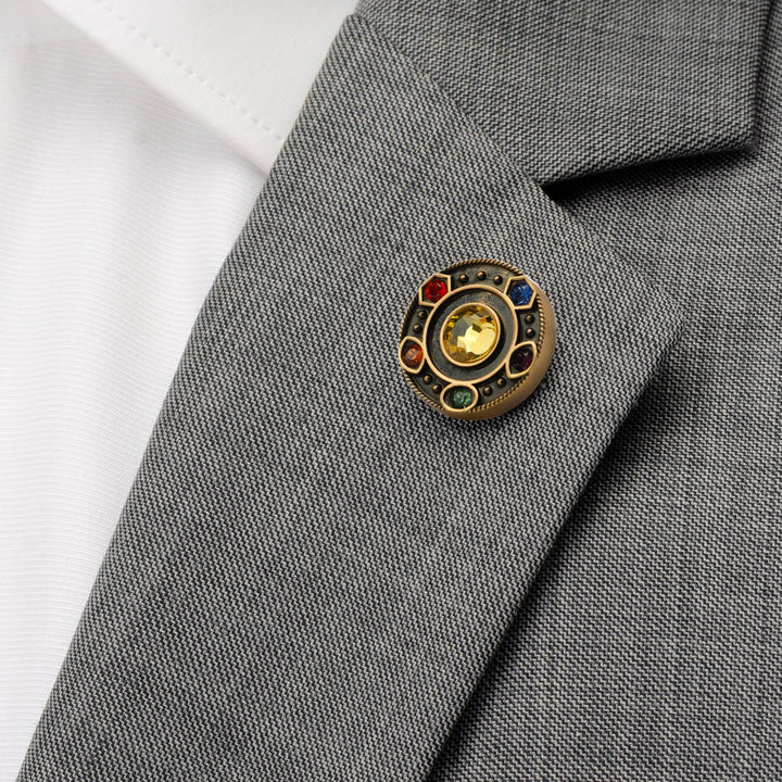 Marvel Avengers Infinity Stones Antique Gold Lapel Pin featuring a circular gold design with six colored stones, pinned to the lapel of a grey suit jacket.