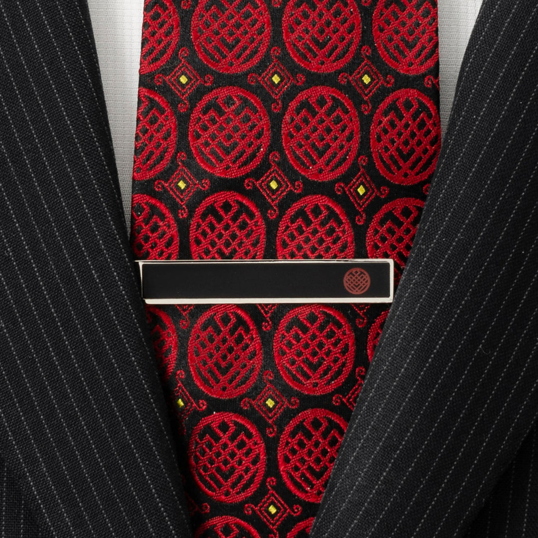 A rectangular black Marvel Shang-Chi Tie Bar featuring a small circular Ten Rings emblem, worn over a red and black patterned tie and black pinstripe suit jacket.