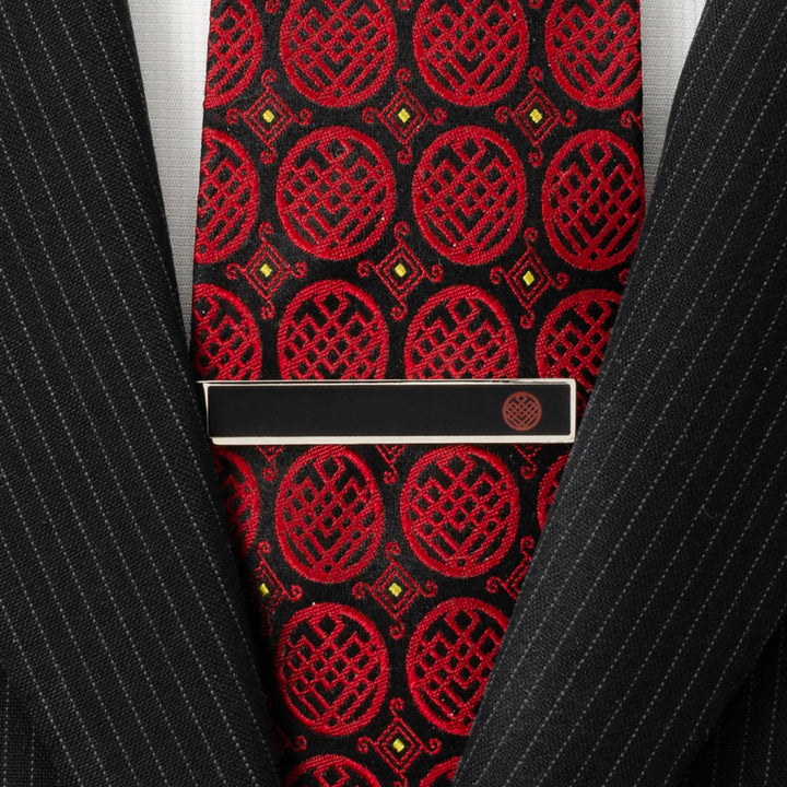 A rectangular black Marvel Shang-Chi Tie Bar featuring a small circular Ten Rings emblem, worn over a red and black patterned tie and black pinstripe suit jacket.