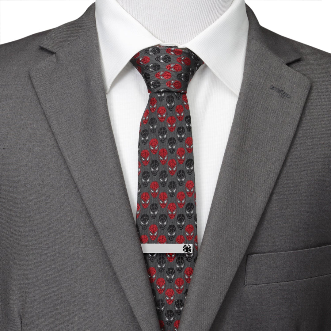 A silver-toned Marvel Spider-Man Spider Tie Bar featuring a small black spider emblem, worn on a dark grey tie with a red and black mask pattern, a white dress shirt, and a grey suit jacket.