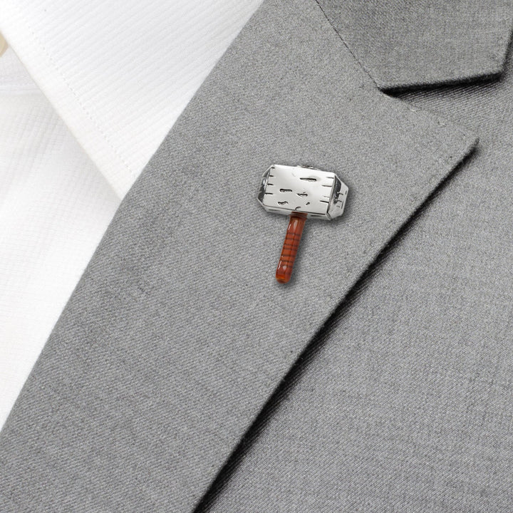 A silver-toned Marvel Thor Mjolnir Lapel Pin with a brown handle attached to the lapel of a grey suit jacket.