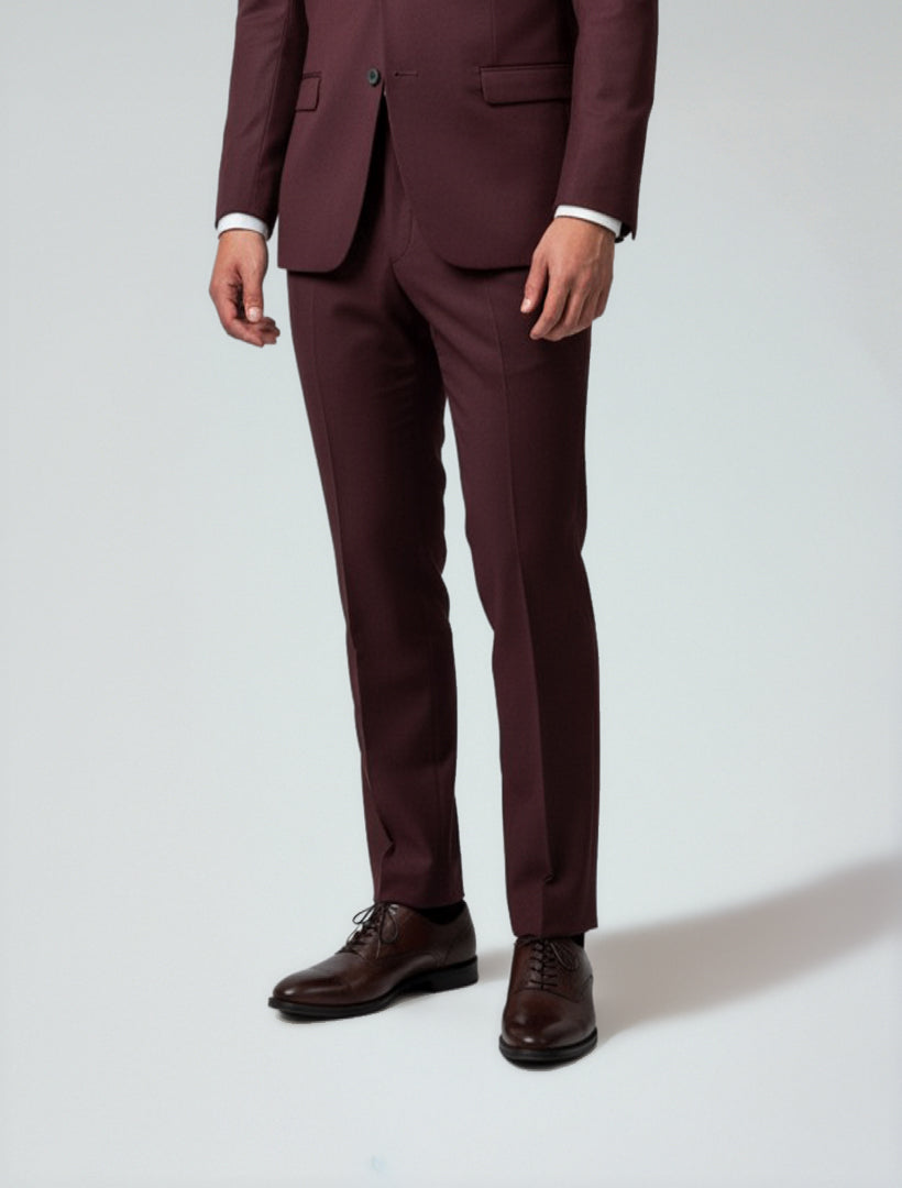 A person wears Couture 1910 Men's Burgundy Dress Pants with brown dress shoes, standing against a plain light background—ideal for a polished, couture-inspired style.