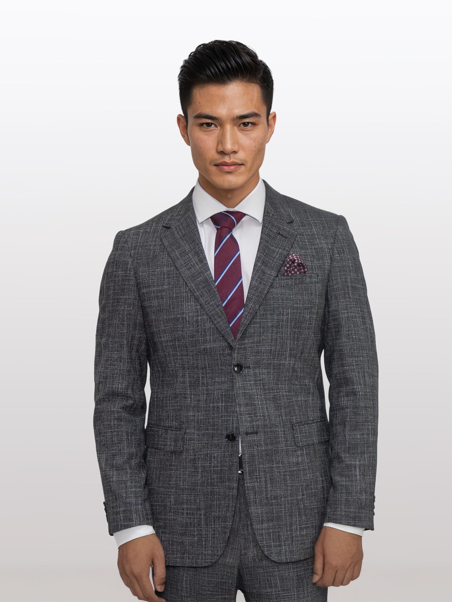 A man confidently stands against a plain background, dressed in Gianco Ferro's Men's Charcoal with Black Pattern Slim Fit Suit. He pairs the suit with a crisp white shirt, a striped tie in red and purple hues, and finishes off the look with an elegant pocket square.