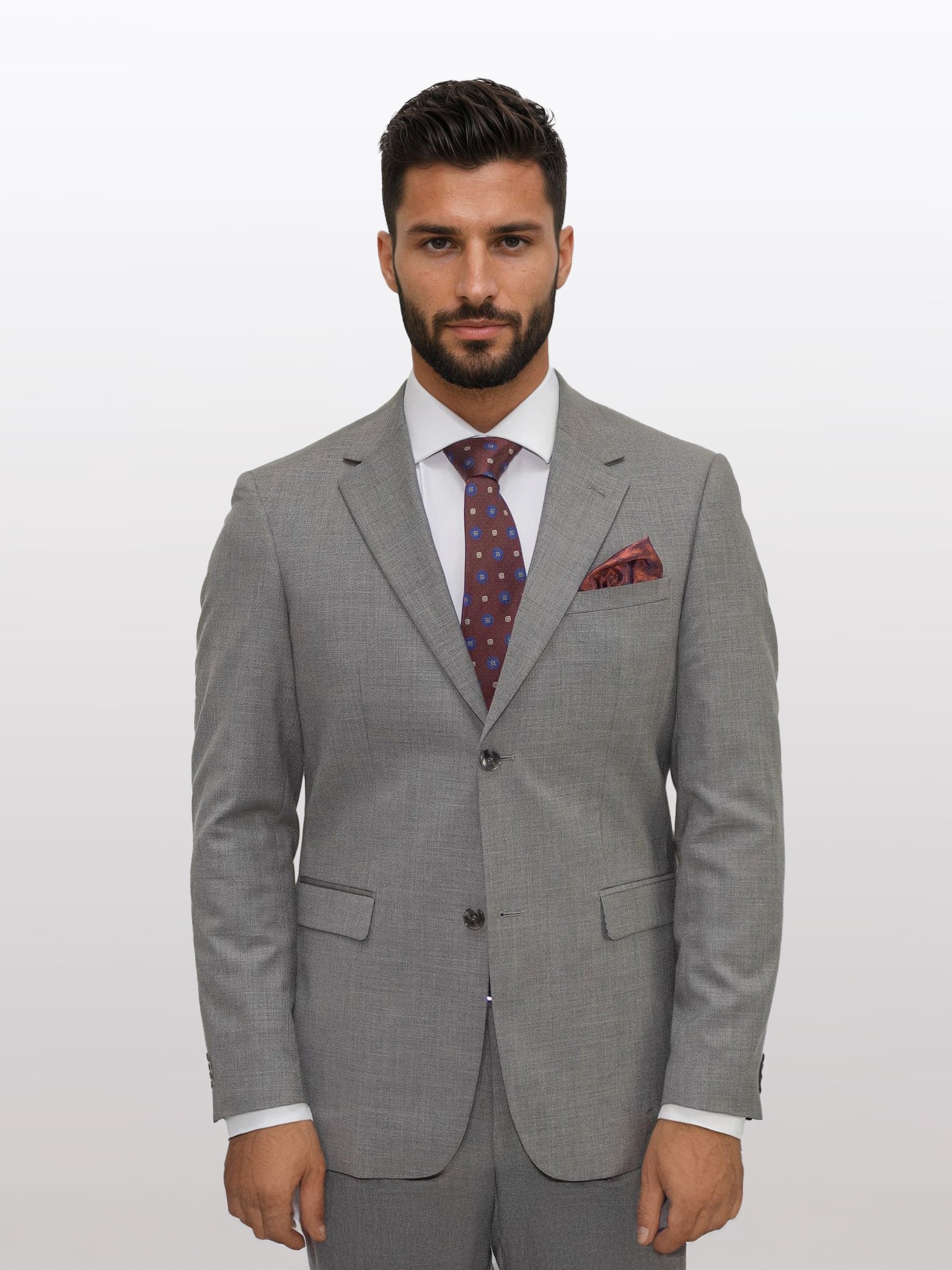 A man styled in a Gianco Ferro Men's Tan Solid Slim Fit Suit, paired with a white shirt, patterned tie, and pocket square, highlighting the stretch armhole design and crafted from tetron rayon, stands against a plain background.