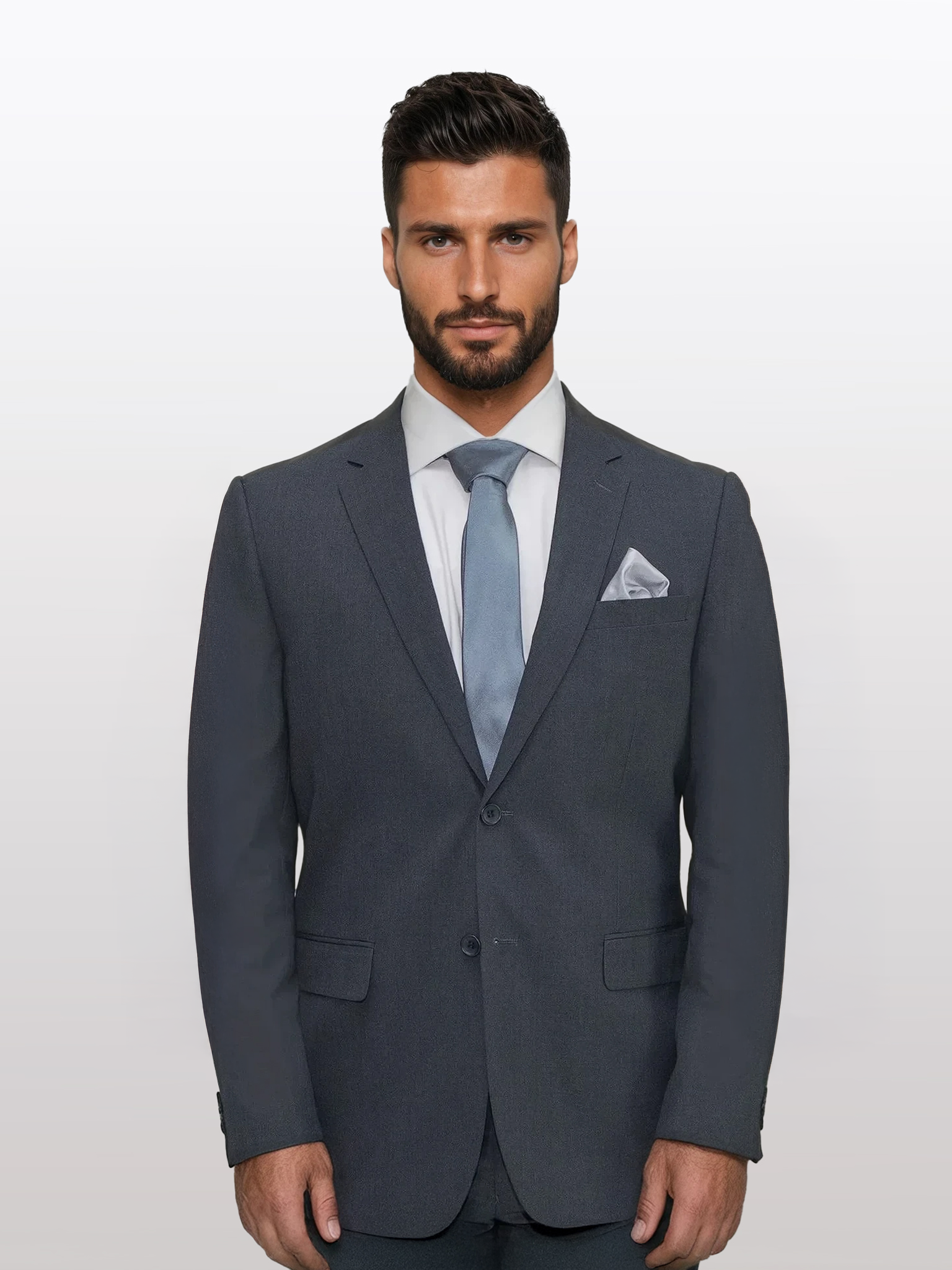 A bearded man dressed in a Karako Men charcoal suit, paired with a light blue tie and a white pocket square, stands against a white background.