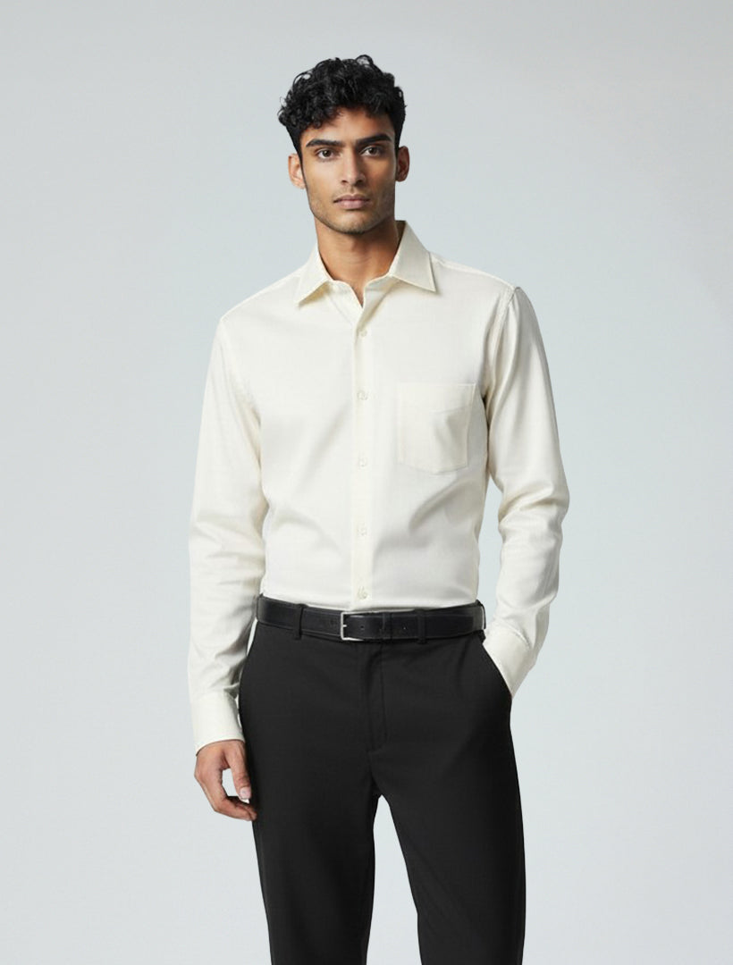 A man faces forward wearing the Karako Men Bone Dress Shirt by Karako Men, a cream-colored classic-fit cotton-polyester shirt, paired with black pants and a black belt against a plain light background.