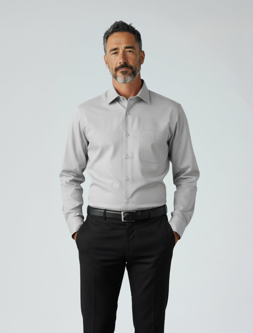 A man stands against a plain background, wearing the Karako Men Light Grey Dress Shirt and black trousers, with his hands in his pockets.