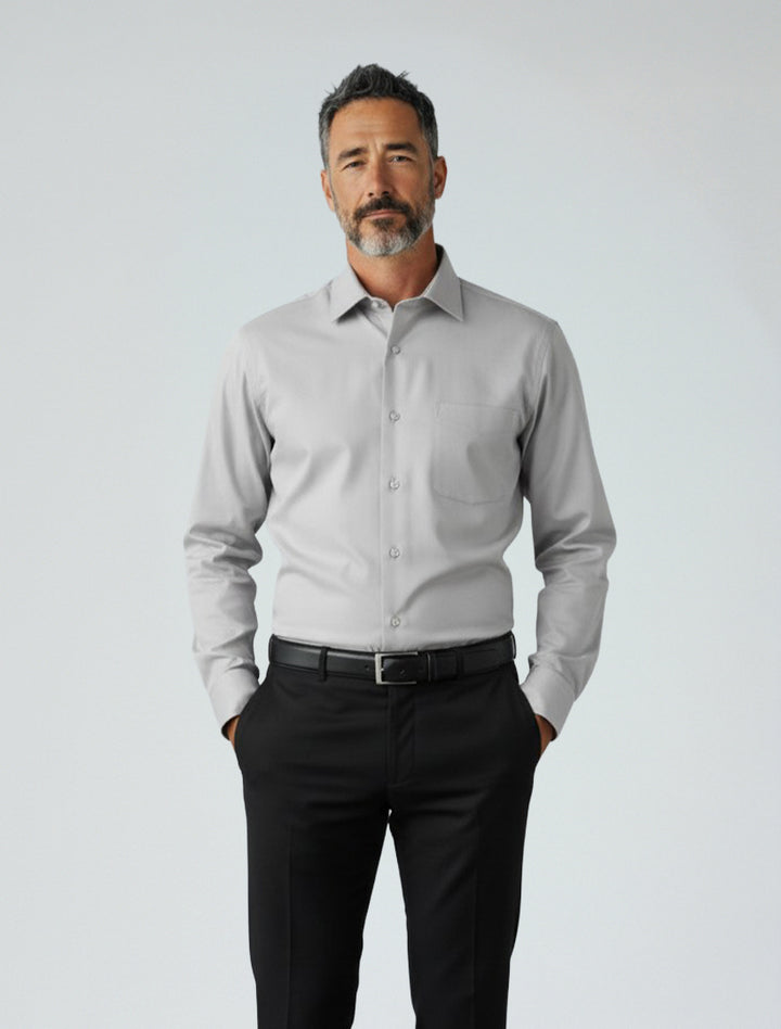 A man stands against a plain background, wearing the Karako Men Light Grey Dress Shirt and black trousers, with his hands in his pockets.