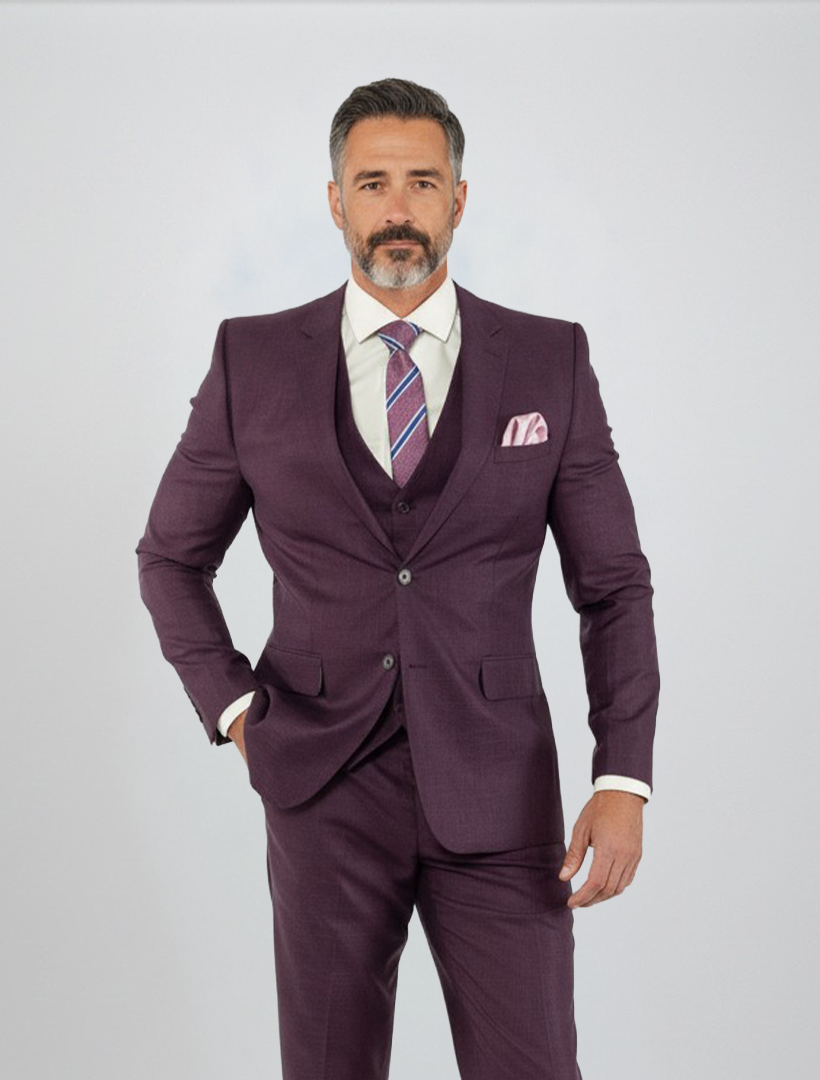 A man with gray hair and a beard models the FUBU Purple Solid Vested Suit from Fubu The Colle—a slim fit, three-piece ensemble styled with a crisp white shirt and striped tie, set against a plain light background.