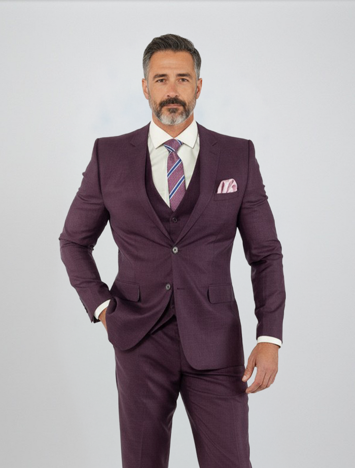 A man with gray hair and a beard models the FUBU Purple Solid Vested Suit from Fubu The Colle—a slim fit, three-piece ensemble styled with a crisp white shirt and striped tie, set against a plain light background.