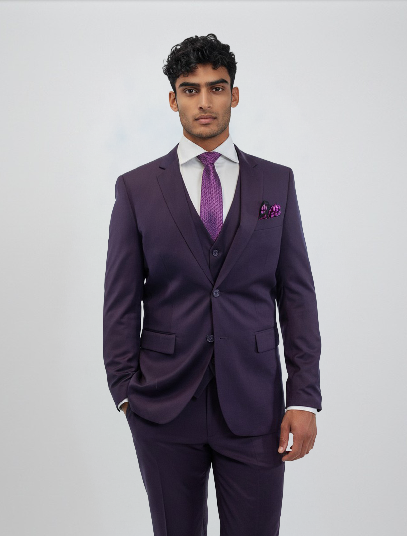 A man models the FUBU Purple Vested Suit by Fubu The Colle, standing against a plain background. He wears the slim fit suit with its matching vest, paired with a white dress shirt, a purple tie, and a coordinating pocket square.