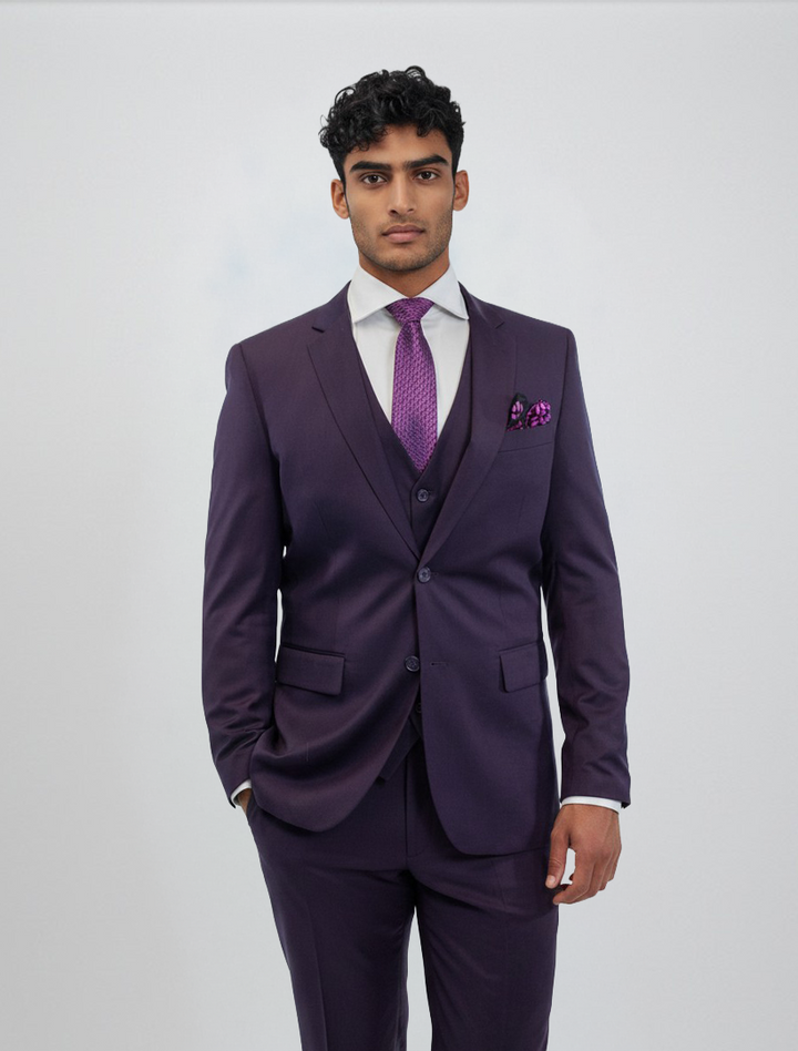 A man models the FUBU Purple Vested Suit by Fubu The Colle, standing against a plain background. He wears the slim fit suit with its matching vest, paired with a white dress shirt, a purple tie, and a coordinating pocket square.
