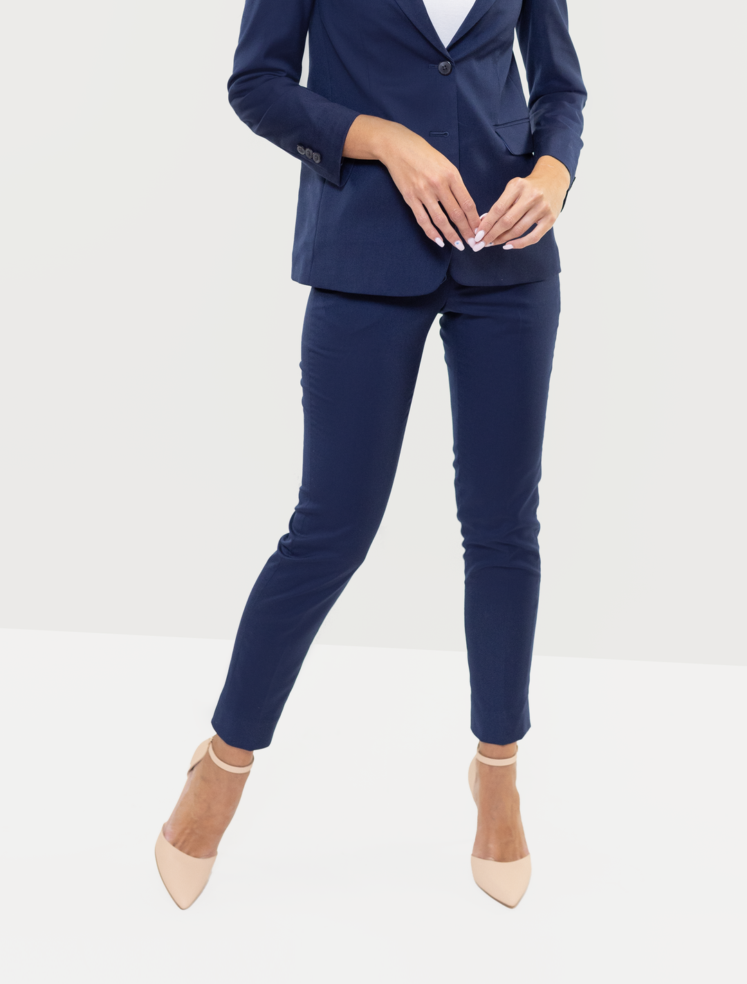 An individual wears the Couture 1910 Women's Navy Suit Separates Pants paired with beige heels, standing against a white background; their face is not visible.