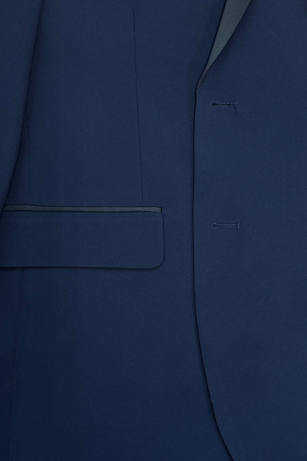 Close-up of the FUBU Classic Notch Lapel Navy Slim-Fit Tuxedo by Fubu The Colle, highlighting its flap pocket, satin notch lapels, and signature two buttonholes.