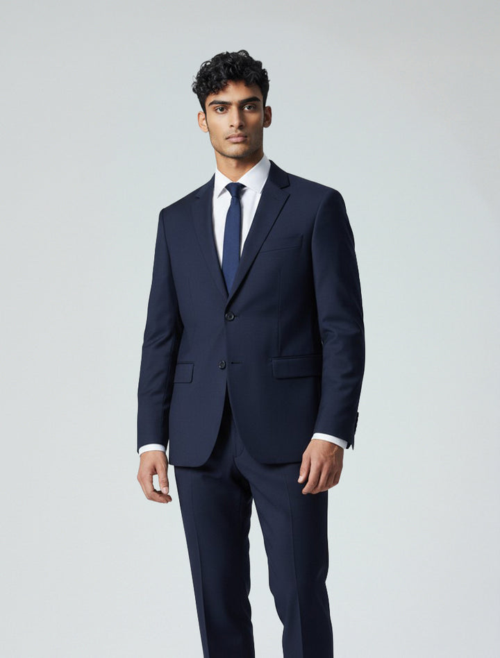 A man in the Karako Men Mens Navy Suit, paired with a white shirt and navy tie, stands against a light background—an ideal, stylish wedding suit choice for men.