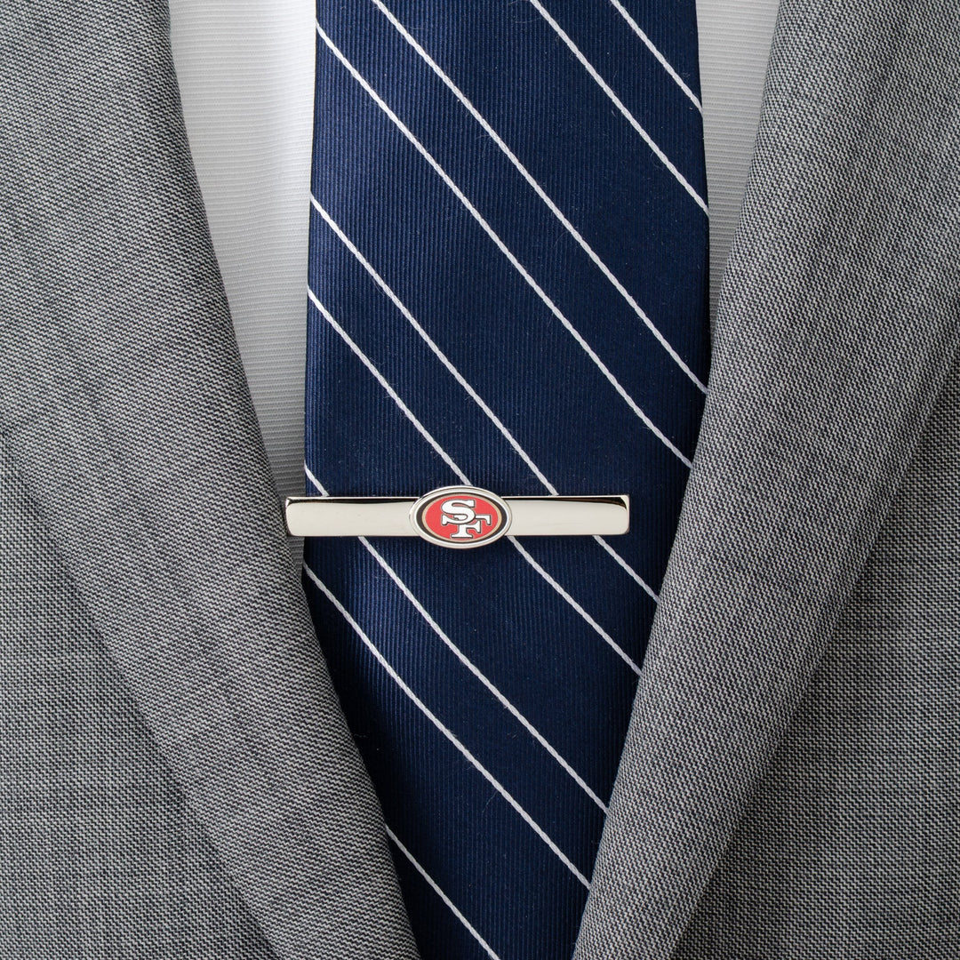 A silver-toned NFL San Francisco 49ers Tie Clip worn over a navy blue striped tie and grey suit jacket.