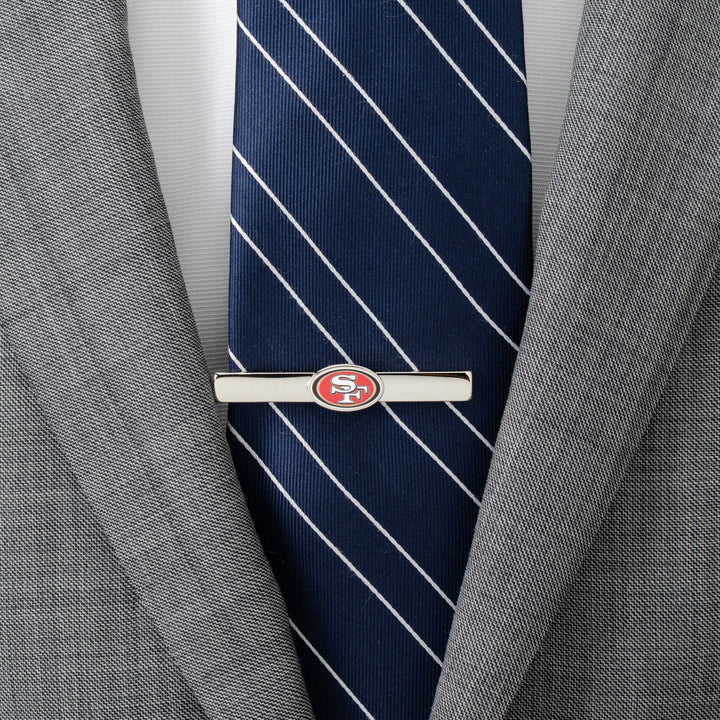 A silver-toned NFL San Francisco 49ers Tie Clip worn over a navy blue striped tie and grey suit jacket.