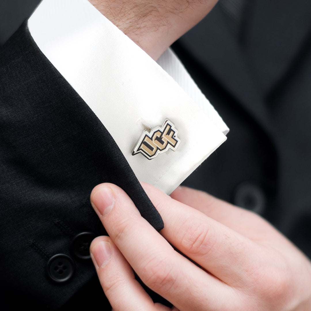 A person in a suit adjusts a gold and black NCAA University of Central Florida Knights Cufflink on a white dress shirt cuff.