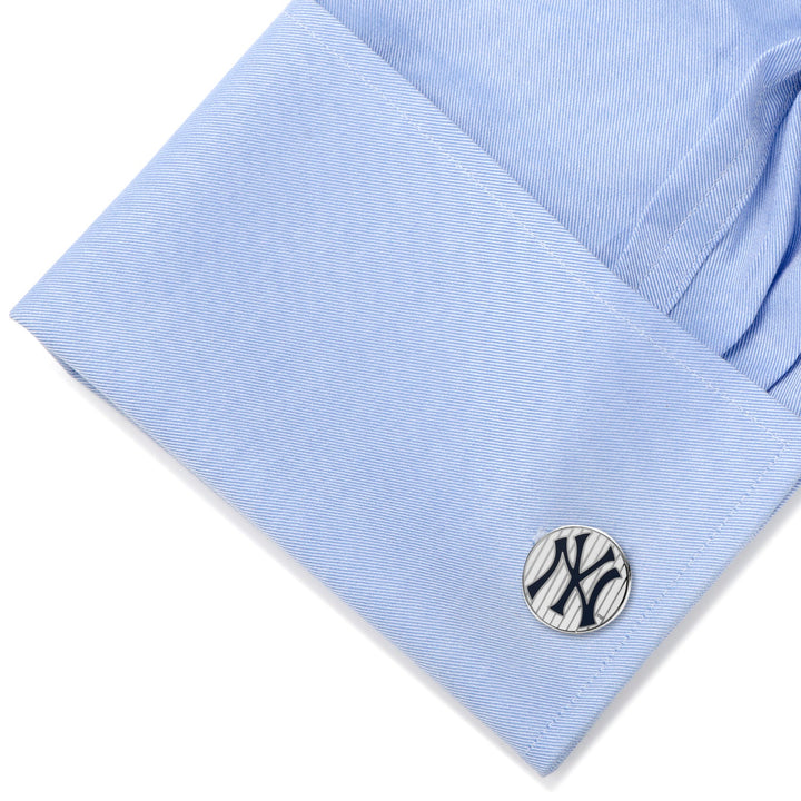 Round silver MLB New York Yankees Pinstripe Cufflinks with a navy blue logo secured on a light blue dress shirt cuff.