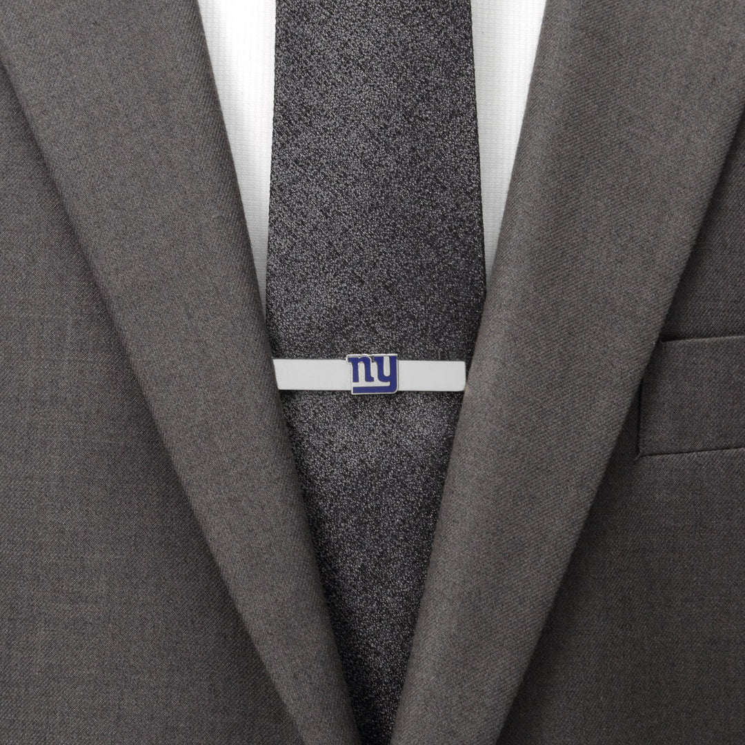 A silver NFL New York Giants Tie Bar featuring the blue “ny” logo, worn on a dark textured tie and grey suit jacket.