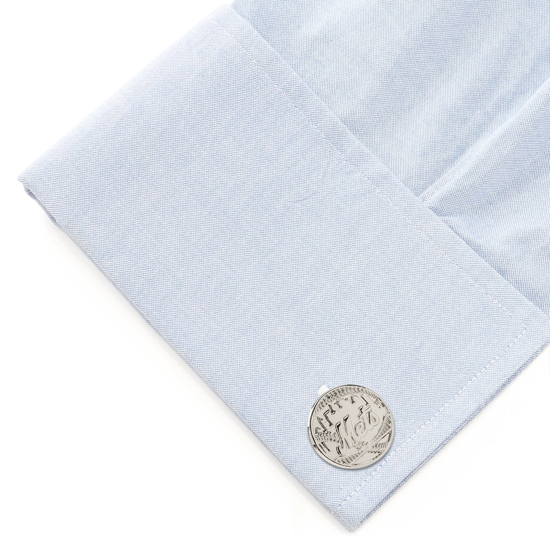 A silver-toned circular MLB New York Mets Silver Edition cufflink attached to a light blue dress shirt cuff.
