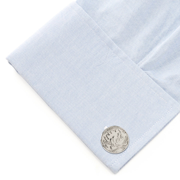 A silver-toned circular MLB New York Mets Silver Edition cufflink attached to a light blue dress shirt cuff.
