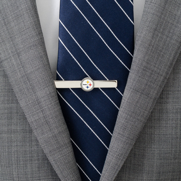 An NFL Pittsburgh Steelers Tie Clip in silver, worn on a blue striped tie and grey suit jacket.
