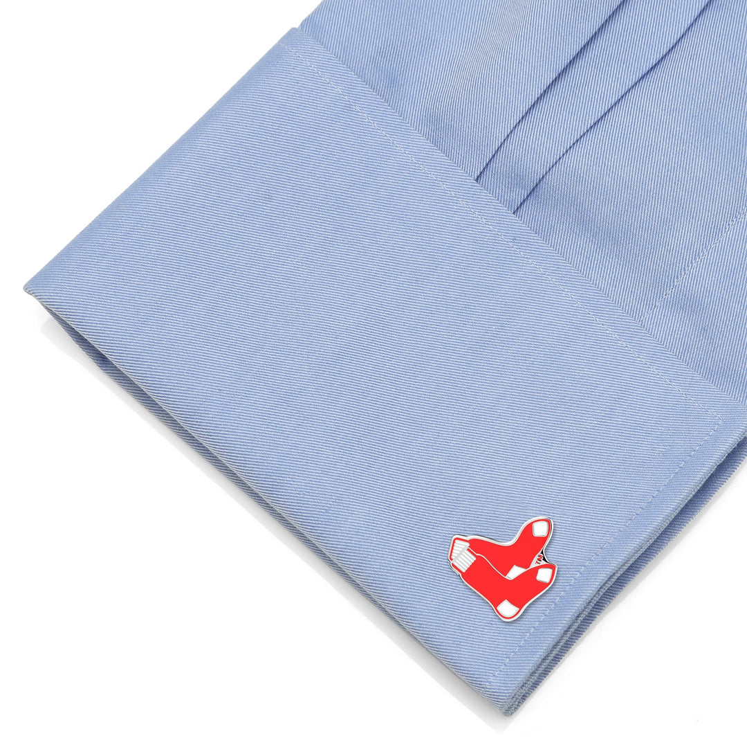 A metal cufflink shaped like a red baseball sock from an MLB Boston Red Sox Cufflinks and Tie Bar Gift Set, attached to a light blue dress shirt cuff.