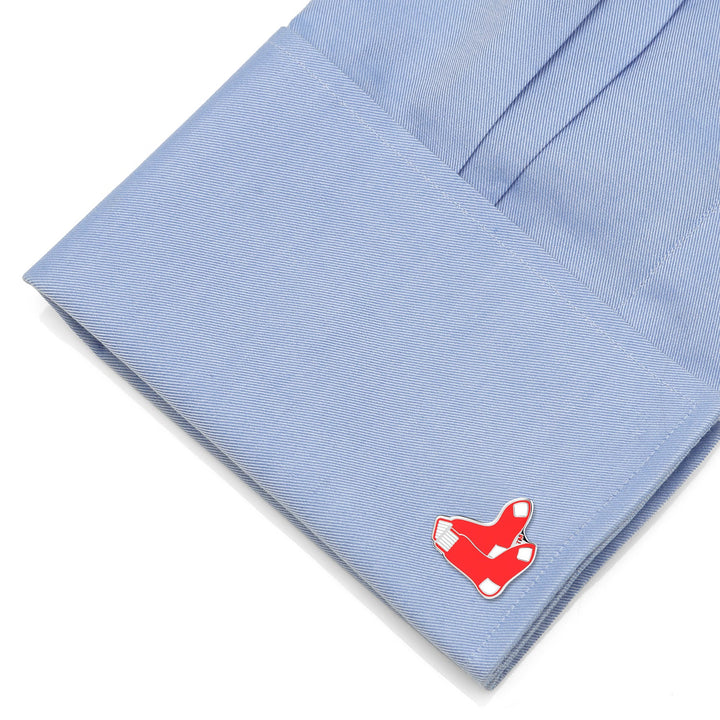 A metal cufflink shaped like a red baseball sock from an MLB Boston Red Sox Cufflinks and Tie Bar Gift Set, attached to a light blue dress shirt cuff.