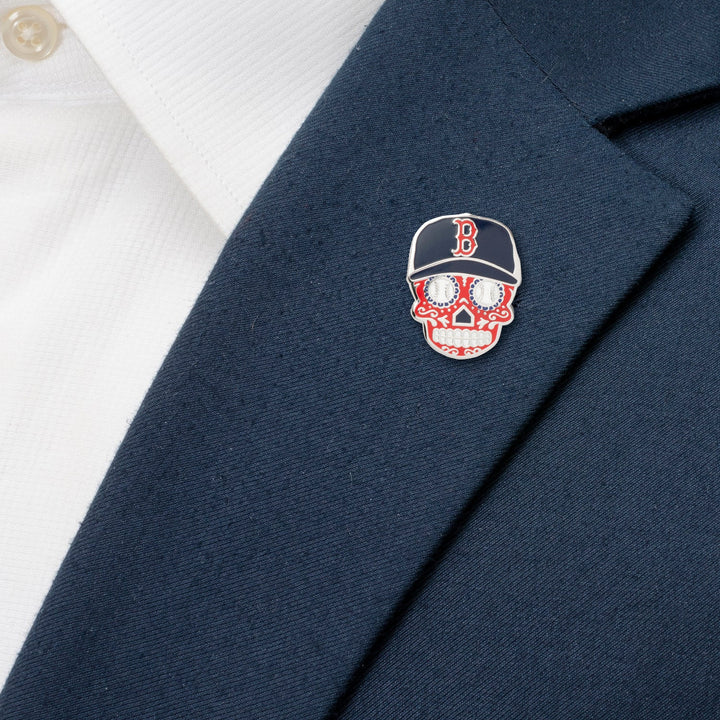 An MLB Boston Red Sox Sugar Skull Lapel Pin shaped like a skull wearing a navy baseball cap with a red “B” logo, attached to a navy blazer over a white shirt.