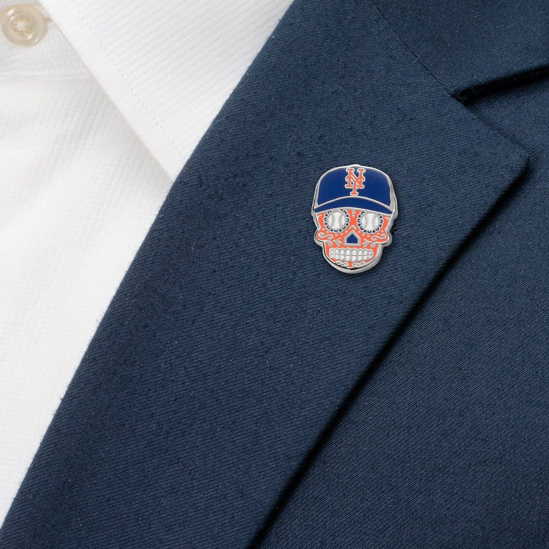 An MLB New York Mets Sugar Skull Lapel Pin, shaped like a sugar skull wearing a New York Mets baseball cap, is pinned to a navy blue suit jacket.