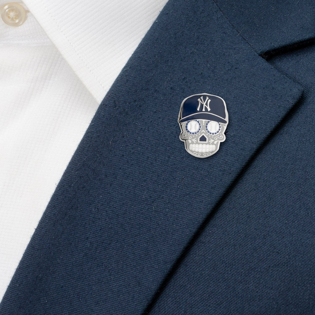 An MLB New York Yankees Sugar Skull Lapel Pin in the shape of a sugar skull wearing a navy blue baseball cap, attached to a navy suit lapel over a white shirt.