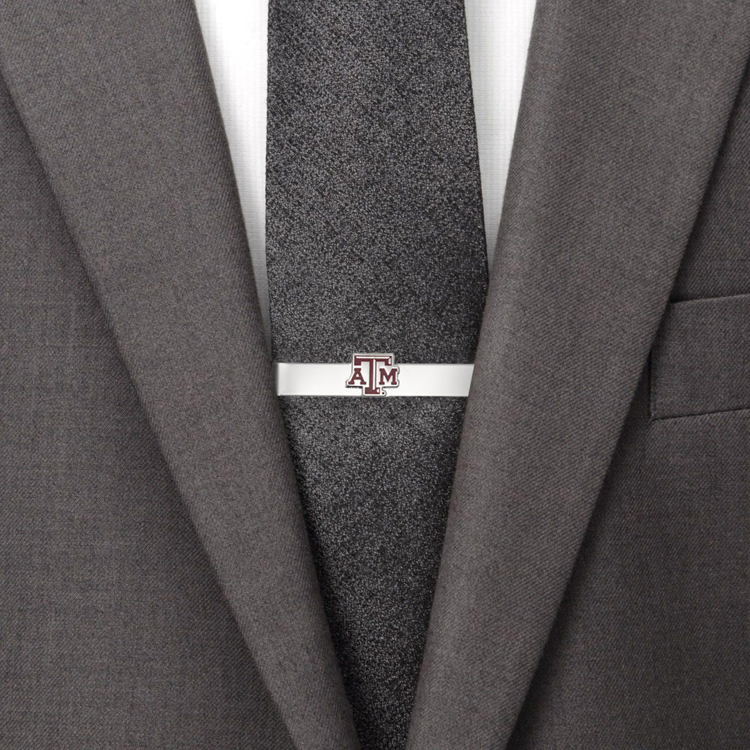 A silver NCAA Texas A&amp;M Aggies Tie Bar featuring the maroon and white logo, worn on a dark textured tie with a grey suit jacket.