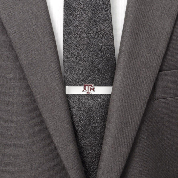 A silver NCAA Texas A&amp;M Aggies Tie Bar featuring the maroon and white logo, worn on a dark textured tie with a grey suit jacket.