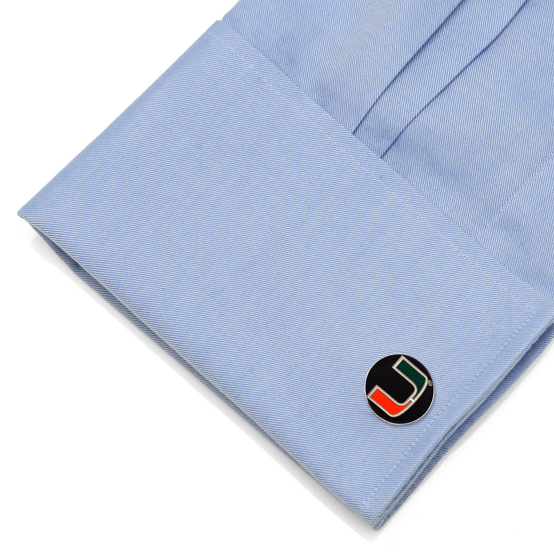Round NCAA Miami Hurricanes Cufflinks featuring the green, orange, and white “U” logo, fastened to a light blue dress shirt cuff.