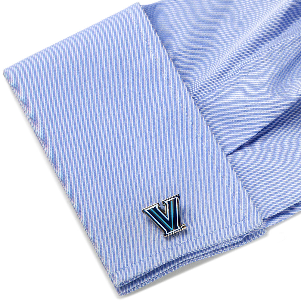 A silver-toned NCAA Villanova Wildcats Cufflinks featuring a blue and white “V” logo fastened to a light blue dress shirt cuff.