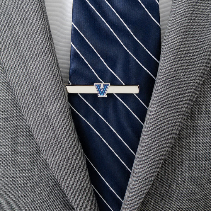 NCAA Villanova University Wildcats tie clip featuring a blue and white V logo, worn on a blue striped tie and gray suit jacket.