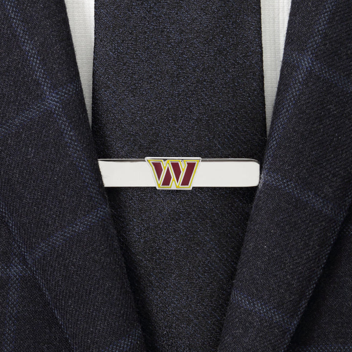 An NFL Washington Commanders Tie Clip featuring a silver “W” logo in burgundy and gold, fastened to a dark blue suit jacket and tie.