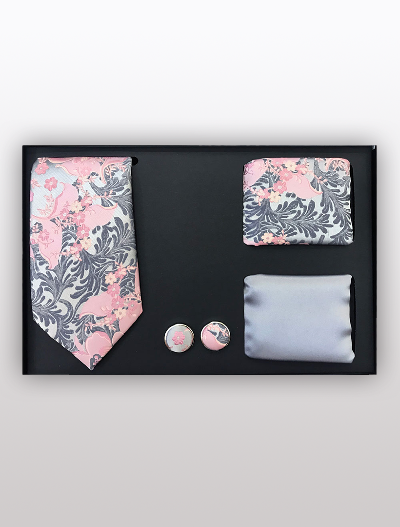 The Men's Four Piece Pink Floral Patterned Gift Box by Vesuvio Napoli includes a slim fit pink and gray floral tie, a matching pocket square, a pair of cufflinks, and an additional solid gray pocket square. Ideal for formal occasions, all items are beautifully packaged in a sleek black gift box.