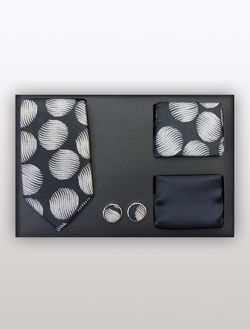 Introducing the Men's Four Piece Black and Grey Circle Patterned Gift Box by Vesuvio Napoli: a sleek set featuring a slim fit tie with black and white polka dots, a coordinating pocket square, an elegant plain black pocket square, and two sophisticated round cufflinks—all beautifully presented in a stylish gift box, ideal for formal occasions.