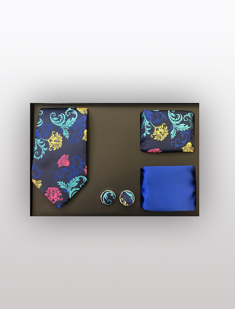 The Men's Four Piece Royal Blue Floral Patterned Gift Box by Vesuvio Napoli includes a Slim Fit Tie, pocket squares, and cufflinks adorned with colorful floral patterns. Ideal for formal events, it is packaged in a sophisticated black gift box.