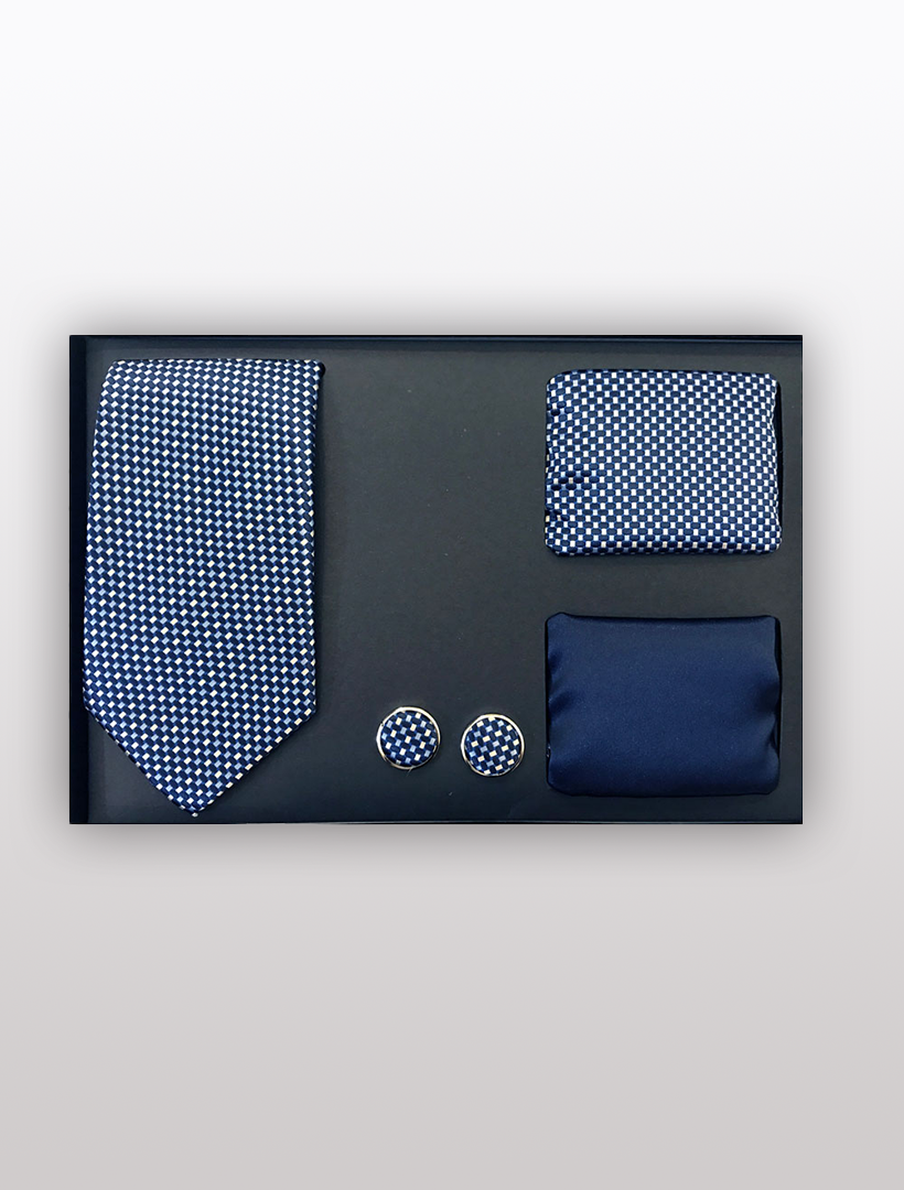 The Men's Four Piece Navy Small Checkered Patterned Gift Box by Vesuvio Napoli includes a slim fit checkered tie, matching pocket square, a solid blue pocket square, and round cufflinks with a similar pattern. These elegant accessories are displayed on a black surface and perfectly presented in a sleek gift box, ideal for the discerning gentleman.