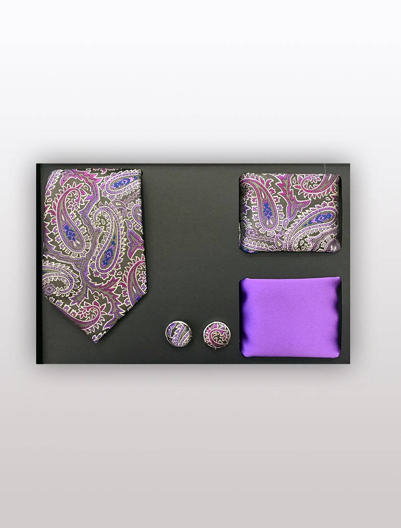 The Men's Four Piece Purple Paisley Patterned Gift Box by Vesuvio Napoli features a slim fit paisley tie, pocket square, cufflinks, and a solid purple handkerchief, all stylishly set against a black background. Elegantly packaged for formal events, it makes the perfect gift.