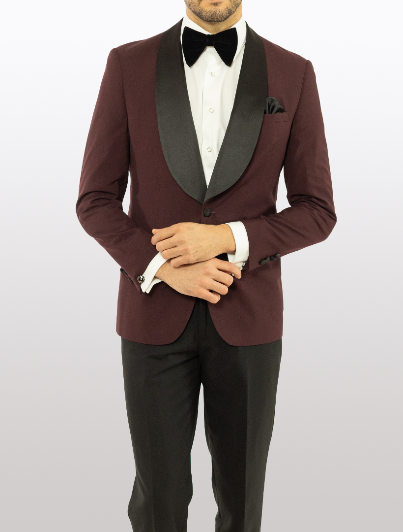 A person elegantly dressed in the FUBU Burgundy Shawl Lapel Slim Fit Tuxedo by Fubu The Colle, complemented by a crisp white shirt and a classic black bow tie.