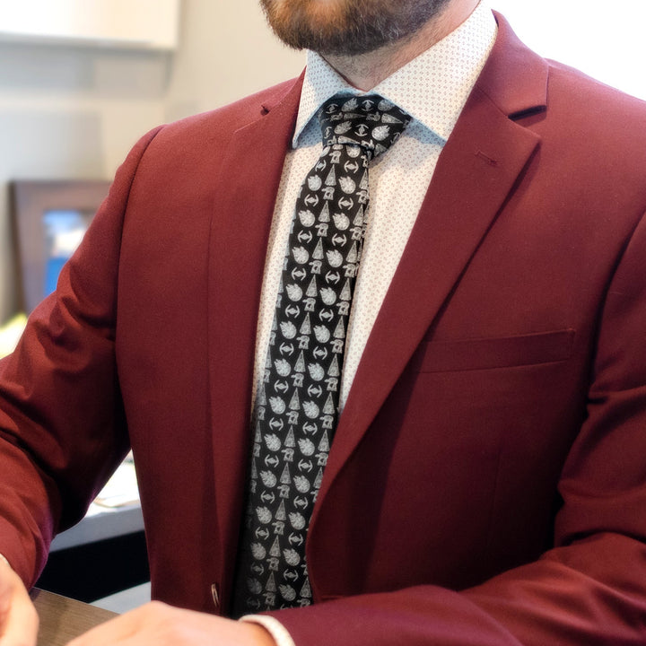 A person wearing a maroon suit jacket and a white patterned shirt with a Star Wars Ships Black Tie featuring a Millennium Falcon print.